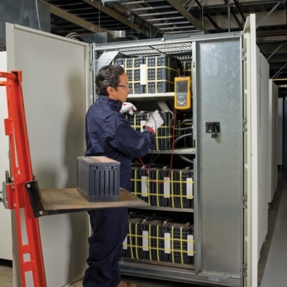 APC technician installing a Batt Manager main system module and fitting a tab washer inside a rack enclosure — alternate view 1